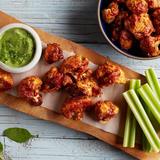 Vegan buffalo cauliflower wings on a serving board with celery and dip