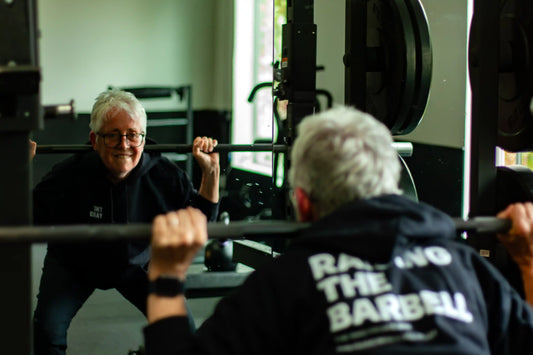 Vegan Nun Sister Pat Farrell, a 72-year-old woman, looks in the mirror and smiles while deadlifting weights, wearing a shirt that says Raising the Barbell